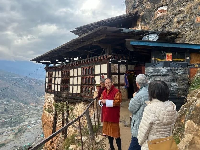 A monk speaking with visitors outside the small monastery building at Drak Karpo, the valley far below