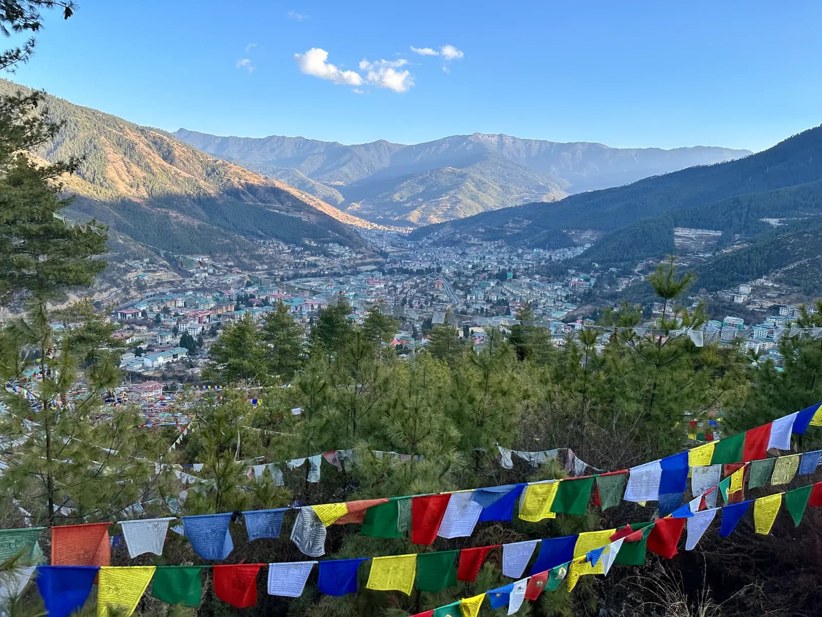 A line of colored prayer flags in the foreground, Thimphu in late afternoon light beyond