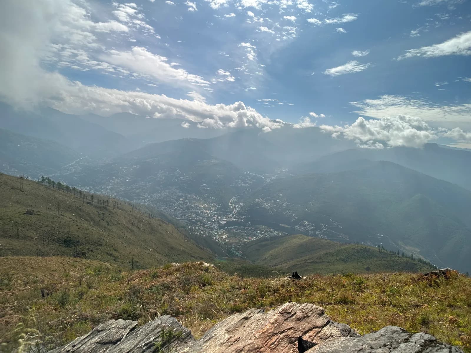 Rock and scrub on a high ridge, sunlight breaking through cloud onto the valley below