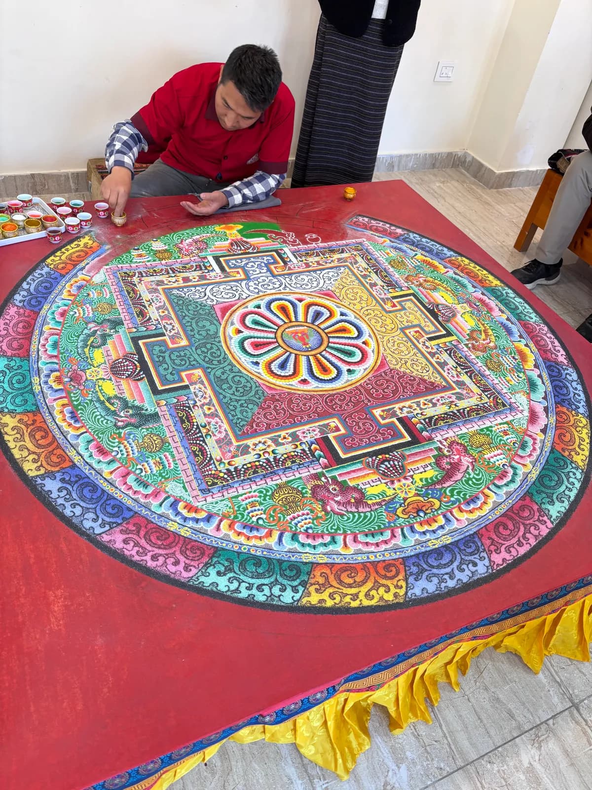 A monk laying colored sand into an intricate mandala on a red table