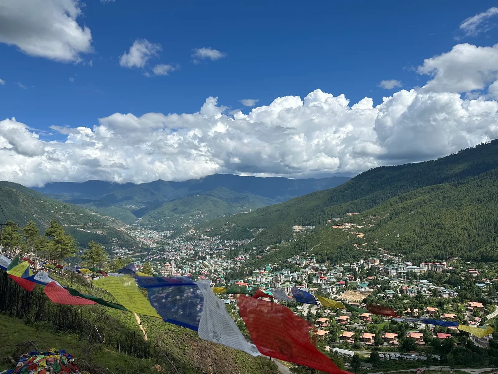 Prayer flags strung across a ridge above the Thimphu valley, the town spread out below under high cloud