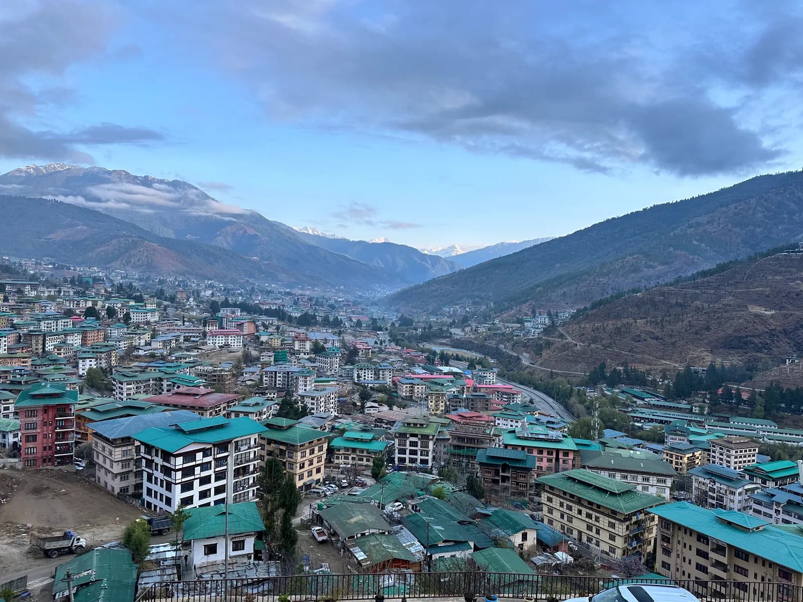 Green and red rooftops of Thimphu at dusk, mountains closing the valley behind