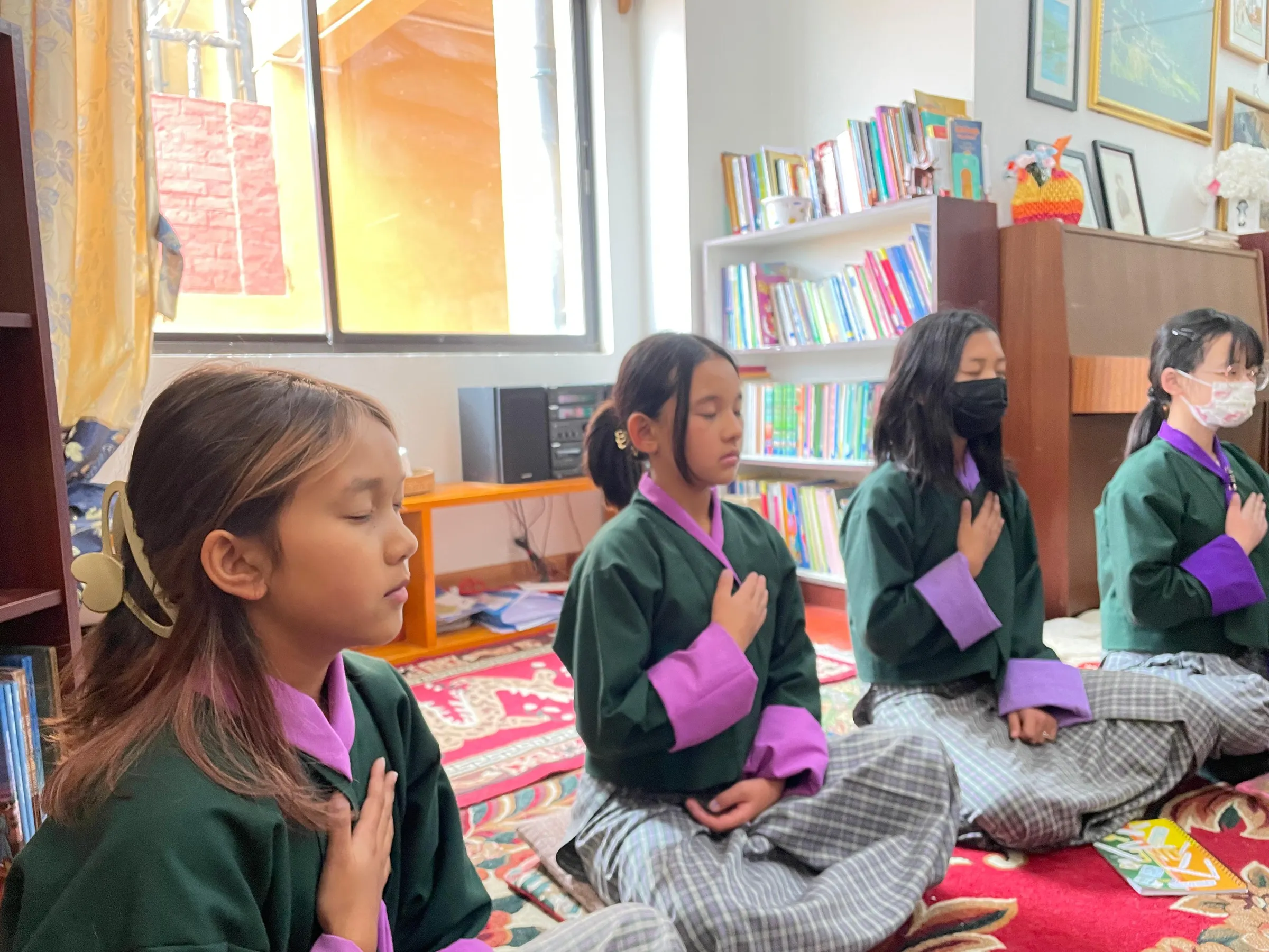 ELC students sitting cross-legged in their classroom during a mindfulness practice, eyes closed and a hand resting over the heart