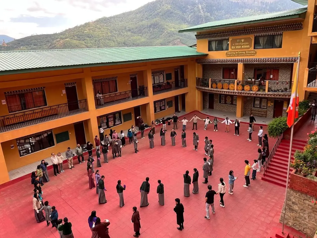 The whole school standing in a circle in the ELC courtyard, hands joined, with the Thimphu hills behind