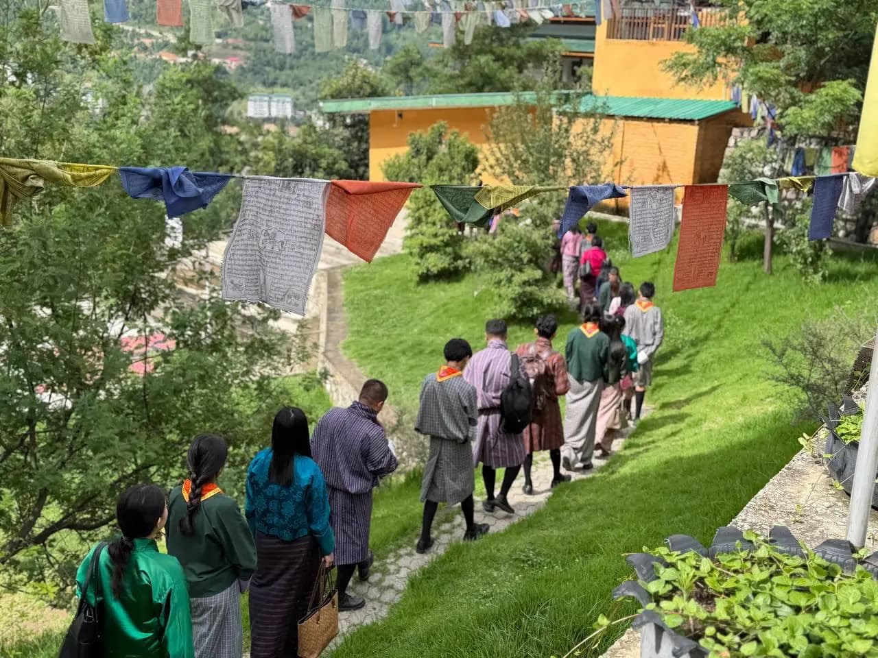 ELC students and teachers walking single file along a grass path under prayer flags