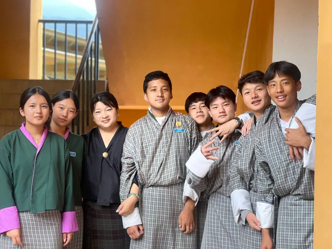 A group of ELC students in traditional gho and kira, with a staff member, smiling together on the school stairwell