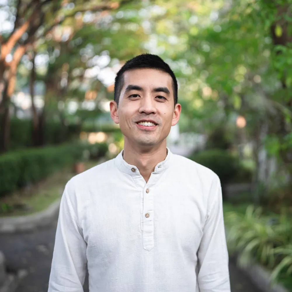 Tim Huang in a white collarless shirt, on a tree-lined garden path