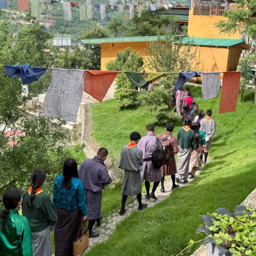 ELC students and teachers walking single file along a grass path under prayer flags during the morning mindful walk