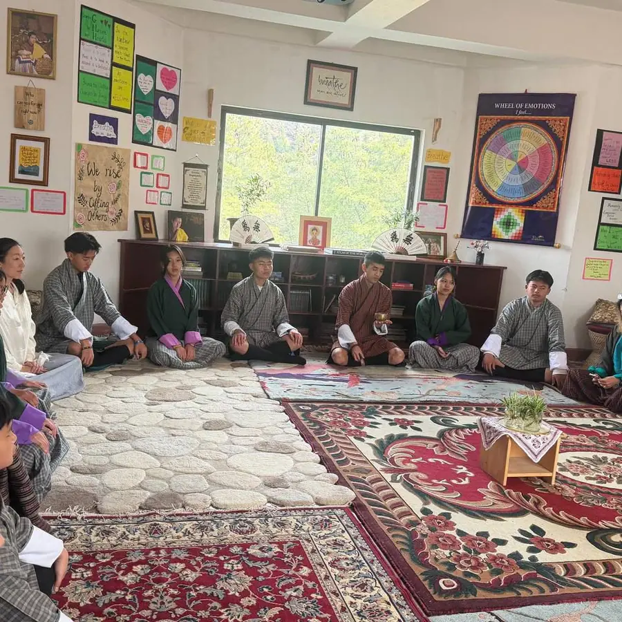 A class seated in a circle on rugs in the wellbeing room, with the teacher sitting among them